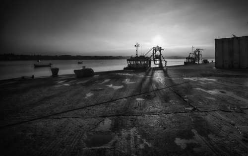 Boats Docked Against A Cement Shore In Black And White Photo