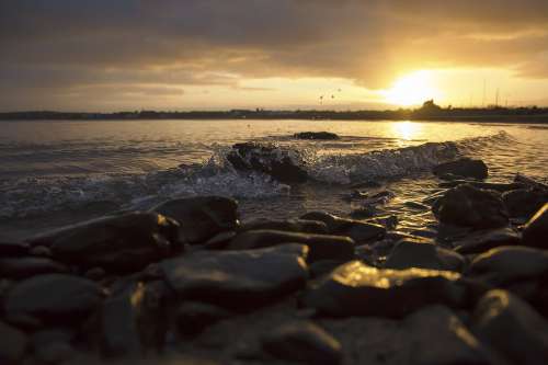 Sunset Against Waves Hitting Rocks On The Shore Photo