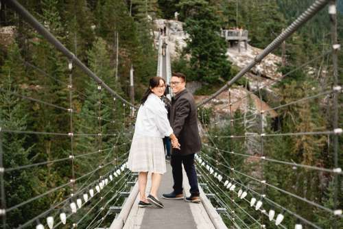 People Hold Hands Walking Down A Suspension Bridge Photo
