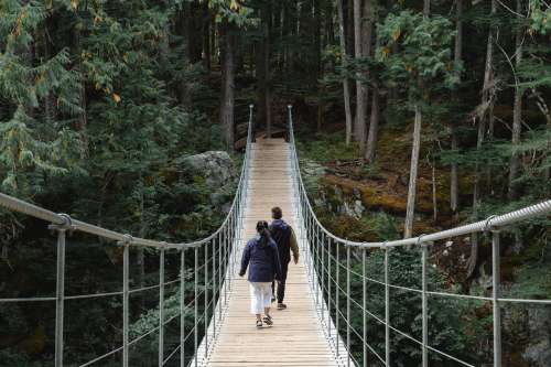 Two People Walk On A Suspension Bridge Towards A Forest Photo