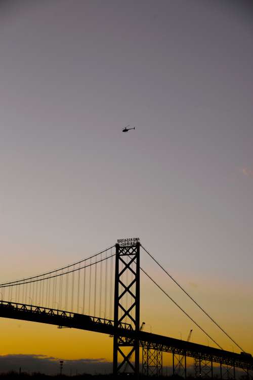 Silhouetted Large Bridge And A Helicopter At Sunset Photo