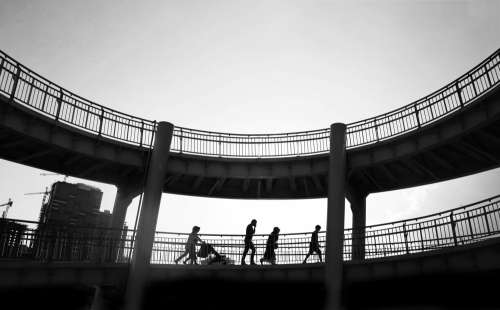 Black And White Photo Of People Walking In A Bridge Photo