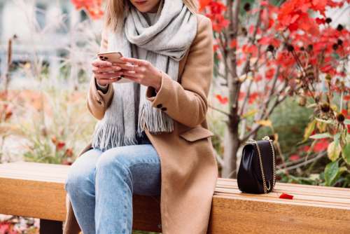 A female sitting on a bench and using her phone on an autumn day