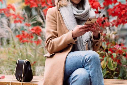 A female sitting on a bench and using her phone on an autumn day 2