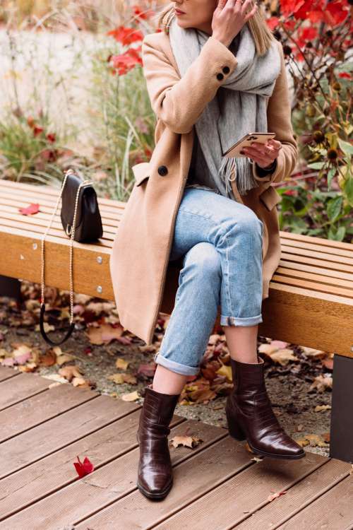 A female sitting on a bench and using her phone on an autumn day 3