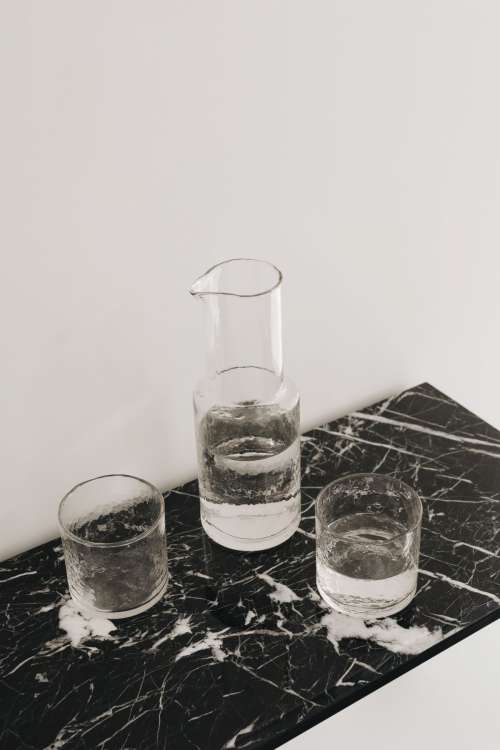 Water in a transparent glass carafe and glasses on a black marble console