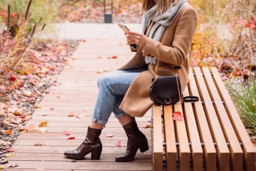 Female sitting on a bench and using her phone on an autumn day 5