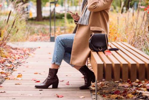 Female sitting on a bench and using her phone on an autumn day 4