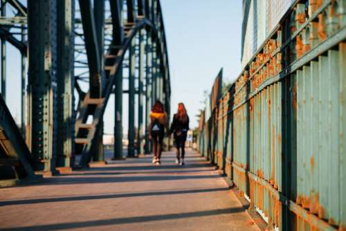 Two females walking across a rusty industrial overpass 2
