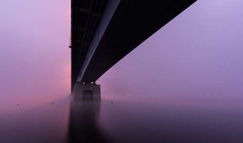 A Bridge Sitting In Thick Pink And Purple Fog Photo