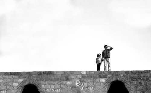 Two People Standing On A Stone Bridge In Black And White Photo