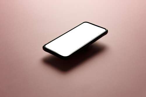 Black Cellphone Floats Above Pink Background Photo