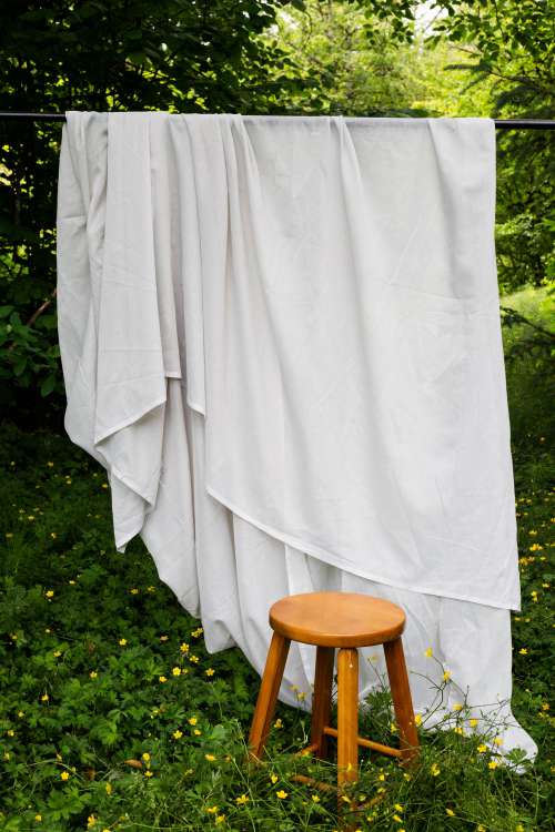 White Flowing Sheet Outdoors With A Wooden Stool In Front Of It Photo