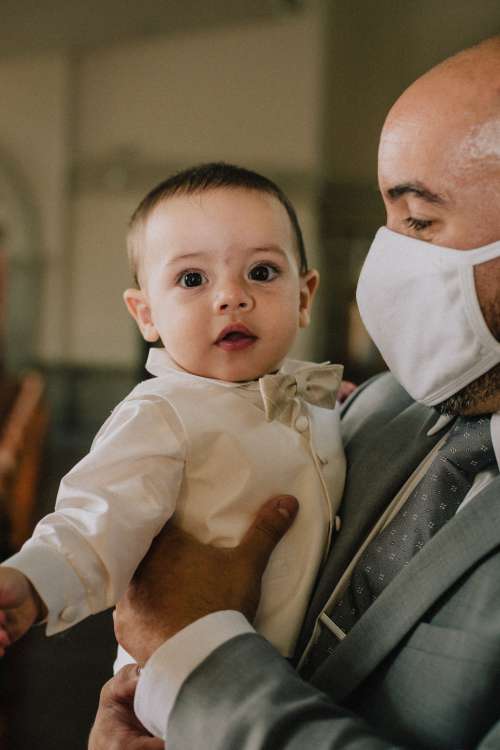 Person In Grey Suit And Facemask Holds A Young Baby Photo