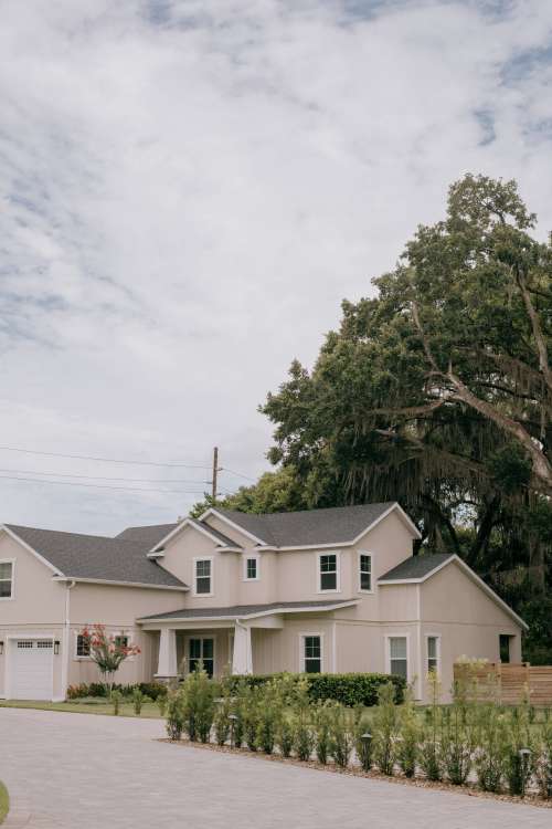 A Beige House With A Grey Roof And Large Trees Photo