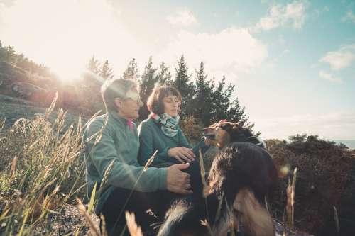 Two People And Their Pet Dog Sit On A Rock In A Hill Photo