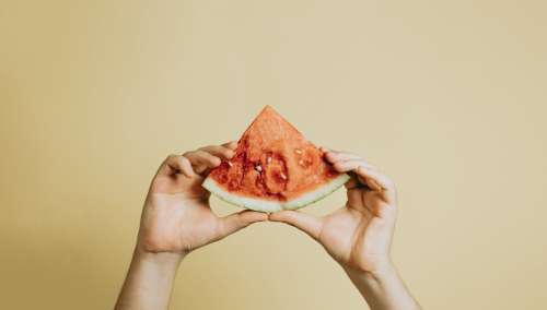 Hands Hold Up A Slice Of Watermelon Against Yellow Photo