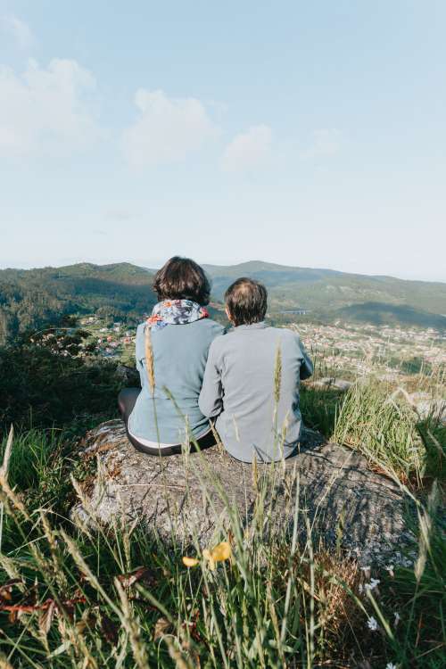 Two People Sitting On Rock Facing Away From Camera Photo