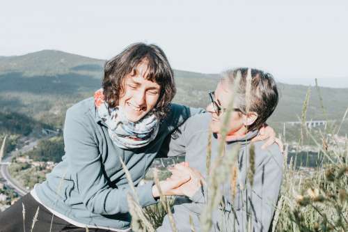 Two Women Laugh Together While Sitting Around Tall Grass Photo