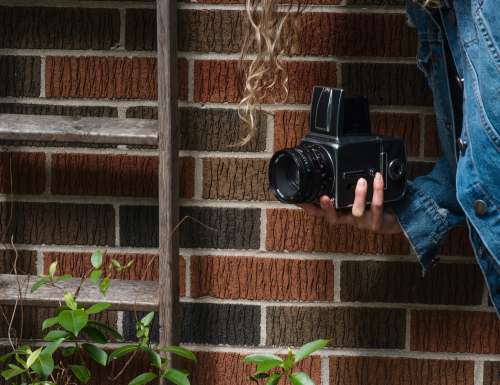 Hand Holds A Hasselblad Camera Standing By A Brick Wall Photo