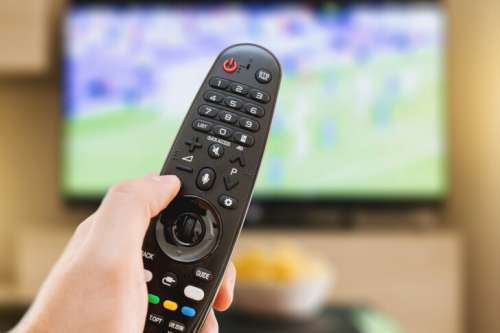 Hand Holding Remote Control with TV Playing in the Background